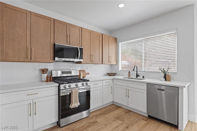 kitchen featuring appliances with stainless steel finishes, a sink, backsplash, light wood finished floors, and light countertops