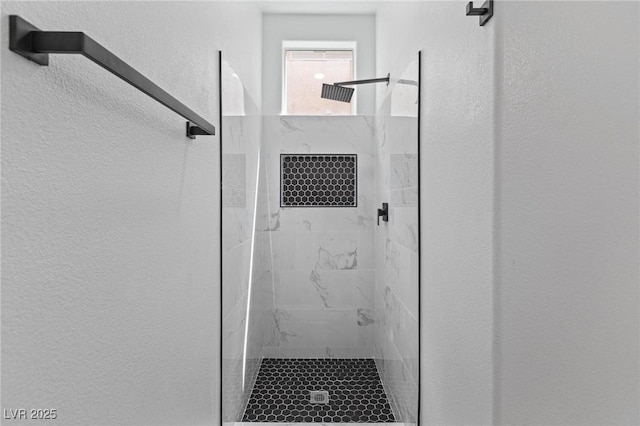 bathroom featuring a textured wall and a tile shower