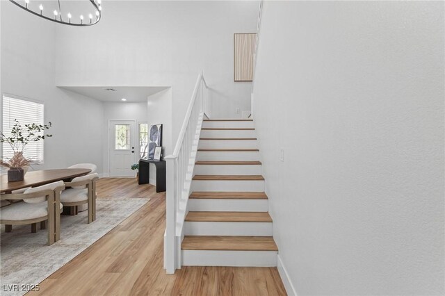 staircase featuring wood finished floors, baseboards, a towering ceiling, and a chandelier