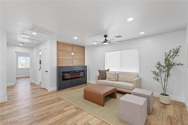 living room with a glass covered fireplace, baseboards, ceiling fan, light wood-style floors, and recessed lighting