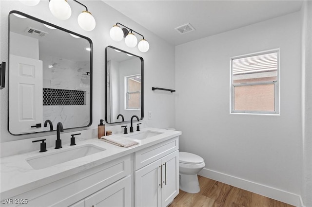 full bath with a shower, toilet, wood finished floors, double vanity, and baseboards