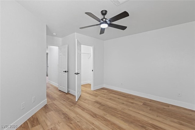 unfurnished bedroom featuring baseboards, light wood-style floors, ceiling fan, a spacious closet, and a closet