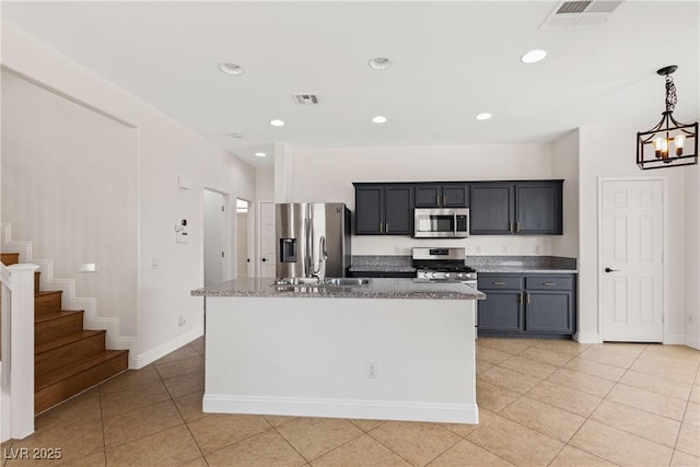kitchen with stainless steel appliances, light tile patterned flooring, an island with sink, a sink, and decorative light fixtures