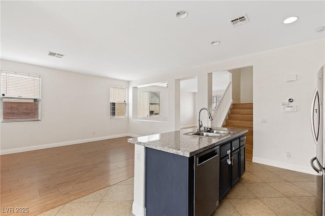 kitchen with a sink, stainless steel appliances, a center island with sink, baseboards, and light stone countertops