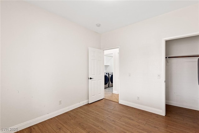 unfurnished bedroom with washing machine and clothes dryer, wood finished floors, baseboards, and a closet