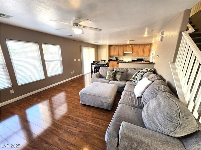 living area with stairs, baseboards, dark wood-type flooring, and a ceiling fan