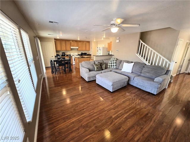 living room featuring dark wood-style floors, ceiling fan, and stairs