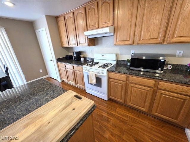 kitchen featuring under cabinet range hood, white range with gas cooktop, stainless steel microwave, dark wood-type flooring, and butcher block countertops