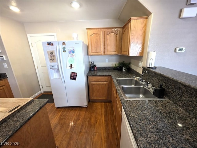 kitchen with white appliances, a sink, dark wood-style flooring, dark stone countertops, and brown cabinets