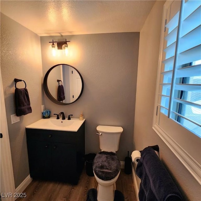 bathroom with wood finished floors, a textured wall, toilet, vanity, and baseboards