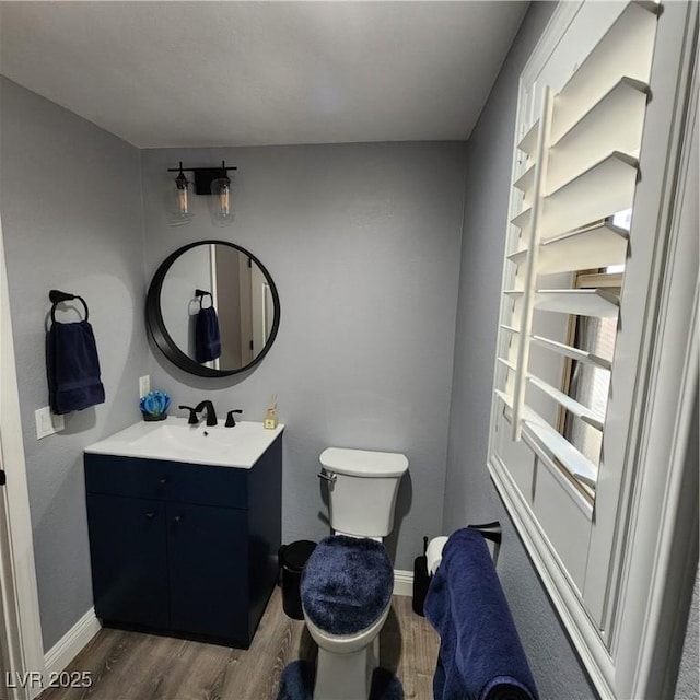 half bath with wood finished floors, toilet, baseboards, and vanity