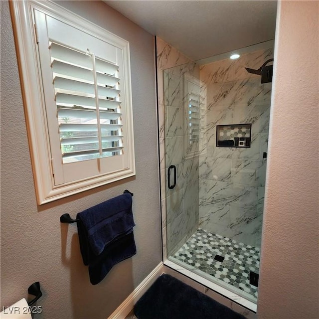 full bath with a marble finish shower and baseboards