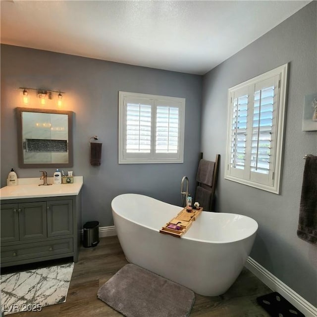 bathroom featuring baseboards, vanity, a freestanding bath, and wood finished floors