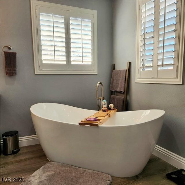 full bathroom featuring baseboards, wood finished floors, and a soaking tub