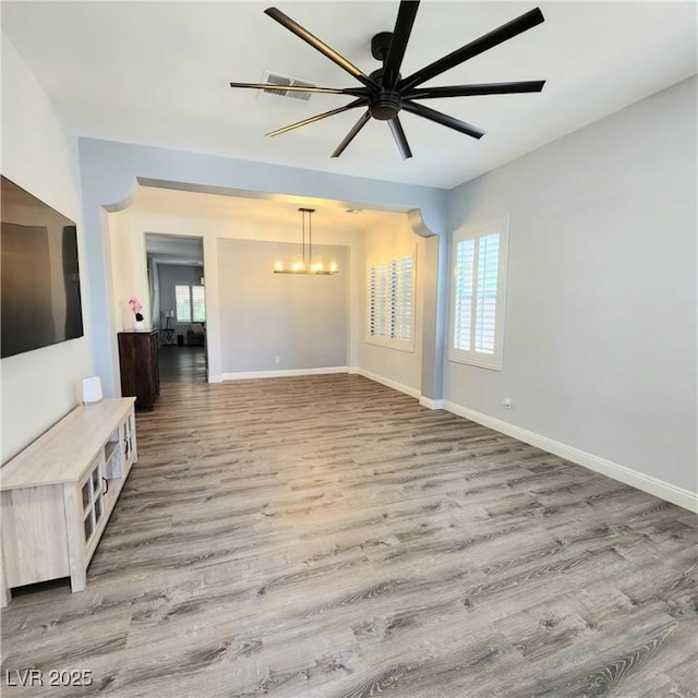unfurnished living room with a chandelier, light wood finished floors, baseboards, and ceiling fan