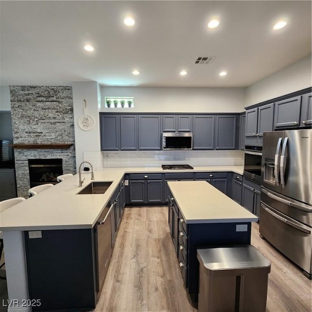 kitchen featuring appliances with stainless steel finishes, a sink, light wood-style floors, light countertops, and a center island