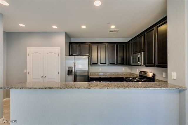kitchen featuring appliances with stainless steel finishes, light stone counters, recessed lighting, a peninsula, and dark brown cabinets