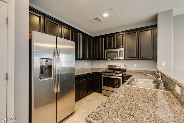 kitchen featuring appliances with stainless steel finishes, a sink, dark brown cabinetry, light stone counters, and recessed lighting