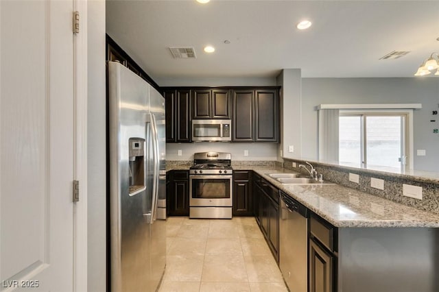 kitchen with stainless steel appliances, a sink, light tile patterned floors, light stone countertops, and recessed lighting