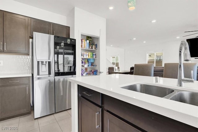 kitchen featuring stainless steel refrigerator with ice dispenser, a sink, light tile patterned floors, light countertops, and dark brown cabinetry
