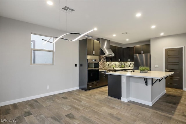 kitchen with stainless steel appliances, wall chimney exhaust hood, light countertops, a sink, and tasteful backsplash