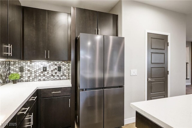 kitchen featuring freestanding refrigerator, light countertops, tasteful backsplash, dark brown cabinetry, and baseboards