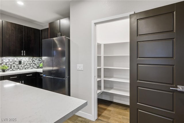 kitchen with stainless steel refrigerator, light countertops, light wood-style floors, decorative backsplash, and dark brown cabinetry