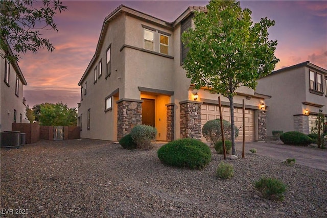 view of front of property featuring stucco siding, stone siding, driveway, fence, and a garage