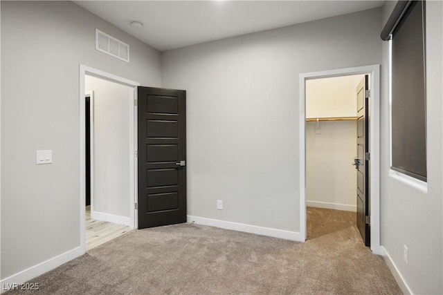 unfurnished bedroom with a walk in closet, carpet flooring, baseboards, and a closet