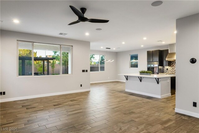unfurnished living room with ceiling fan, wood finished floors, baseboards, and recessed lighting