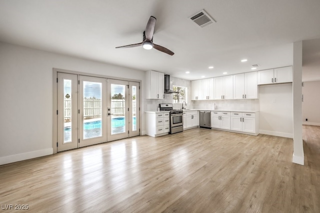 kitchen featuring appliances with stainless steel finishes, french doors, wall chimney range hood, a ceiling fan, and light countertops