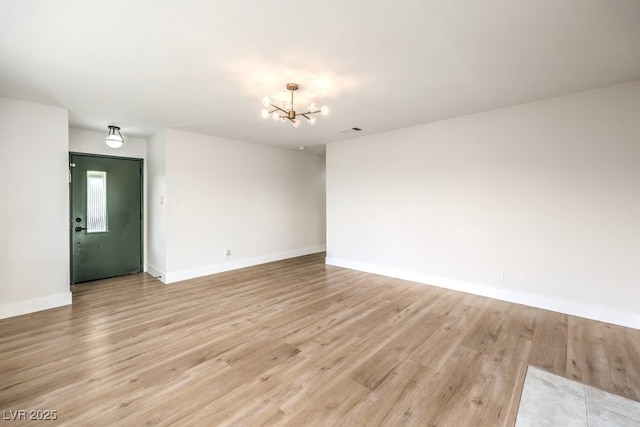 spare room featuring a chandelier, light wood-style floors, and baseboards