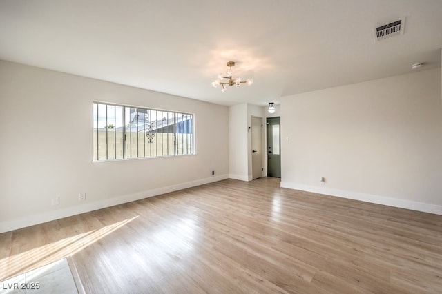 spare room featuring a chandelier, light wood-style floors, and baseboards