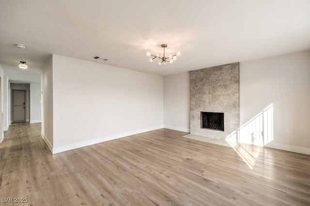 unfurnished living room featuring a chandelier, light wood finished floors, a tile fireplace, and baseboards