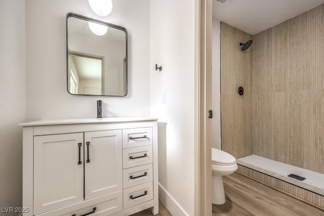 full bath with a tile shower, wood finished floors, toilet, and vanity