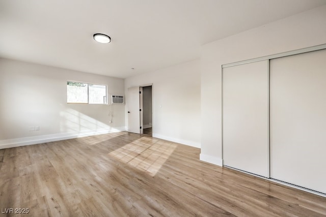 unfurnished bedroom with wood finished floors, a wall unit AC, a closet, and baseboards
