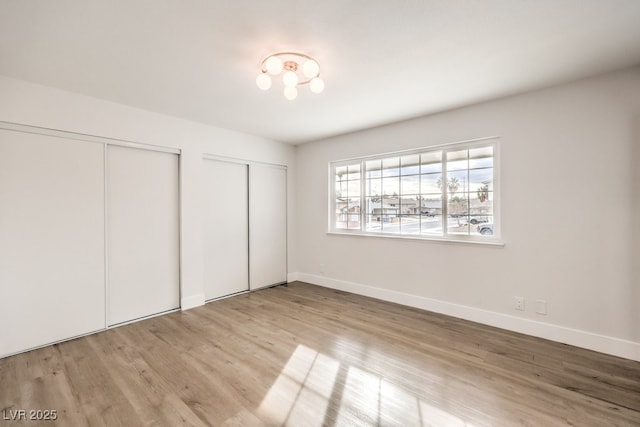 unfurnished bedroom with multiple closets, wood finished floors, and baseboards