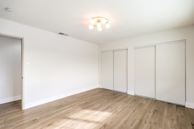 unfurnished bedroom with multiple closets, light wood finished floors, and baseboards