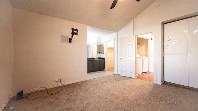 unfurnished bedroom featuring washer and clothes dryer, light colored carpet, connected bathroom, vaulted ceiling, and baseboards