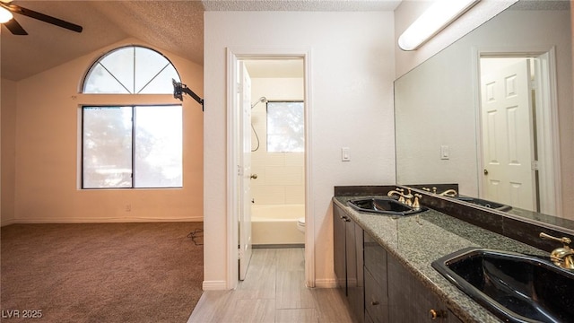 bathroom with a textured ceiling, ceiling fan, double vanity, baseboards, and vaulted ceiling