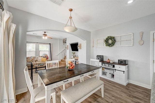 dining room featuring arched walkways, a ceiling fan, wood finished floors, and stairway
