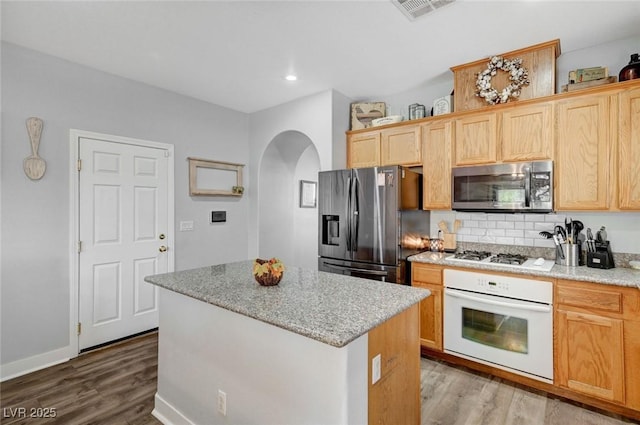kitchen with white appliances, arched walkways, wood finished floors, a center island, and recessed lighting