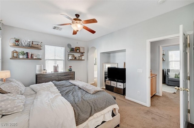 bedroom with multiple windows, light colored carpet, arched walkways, and a ceiling fan