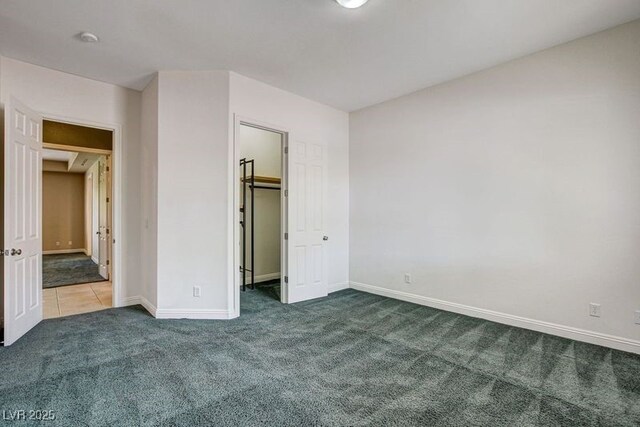 unfurnished bedroom with dark colored carpet, baseboards, and a walk in closet