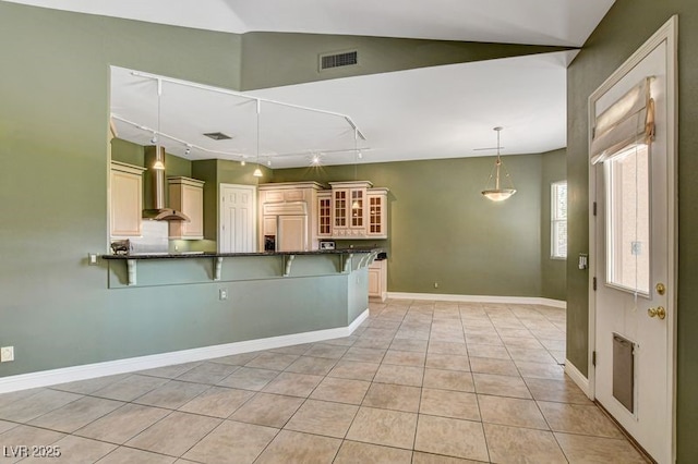 kitchen with wall chimney range hood, a breakfast bar area, dark countertops, paneled built in fridge, and track lighting