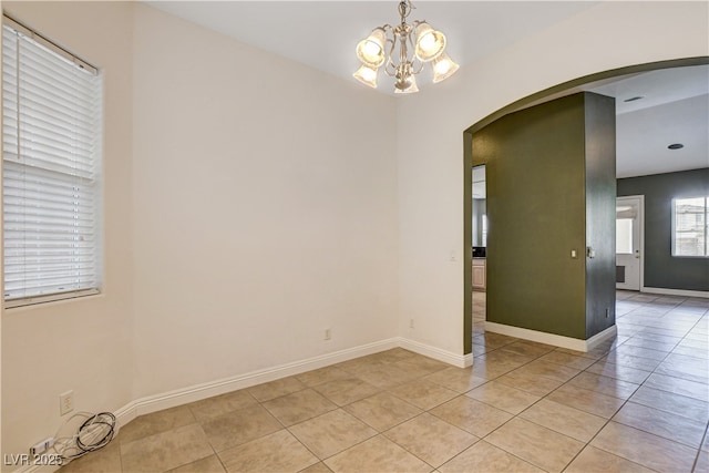empty room with a chandelier, arched walkways, light tile patterned floors, and baseboards