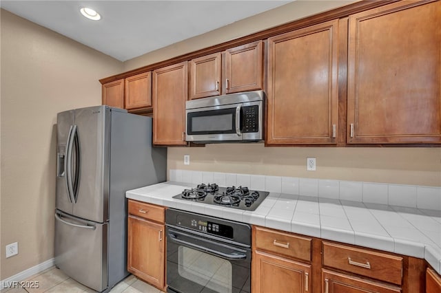 9893 Santa Ponsa Ct, Las Vegas, NV 89178 - kitchen with black appliances, brown cabinets, baseboards, light tile patterned floors, and tile counters