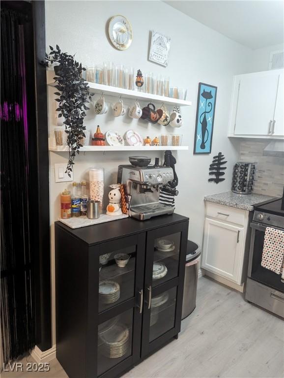212 Orland St Unit 22, Las Vegas, NV 89107 - kitchen with stainless steel range with electric cooktop, white cabinets, light wood finished floors, and backsplash
