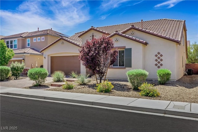 mediterranean / spanish-style home featuring a tile roof, central air condition unit, an attached garage, stucco siding, and driveway