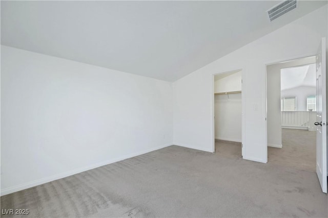 unfurnished bedroom with lofted ceiling, light carpet, baseboards, a closet, and a walk in closet